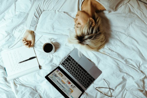 Woman sleeping on bed with laptop and coffee and notebook